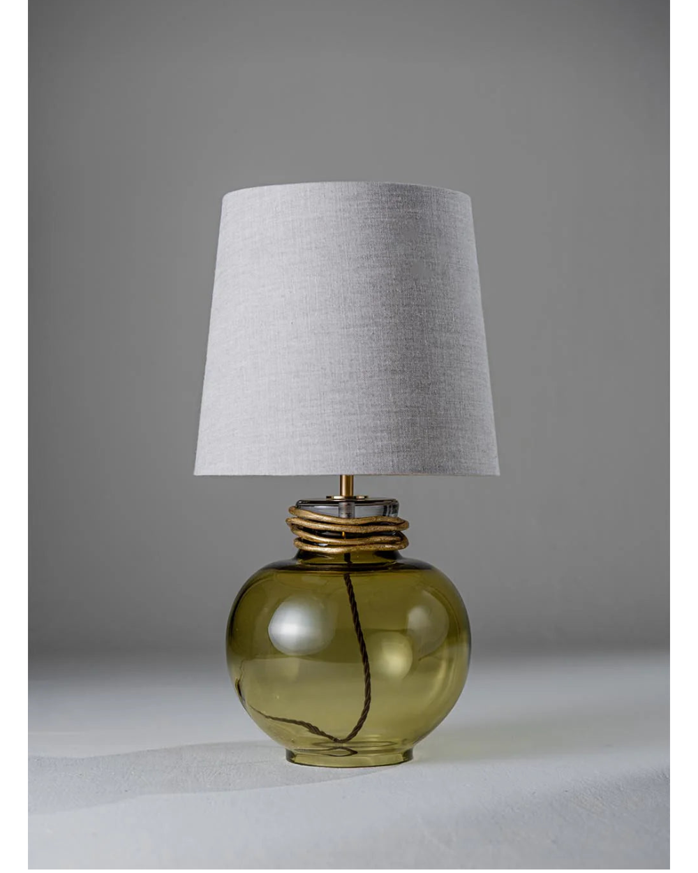 Table lamp with a green glass base and gray lampshade on a neutral background